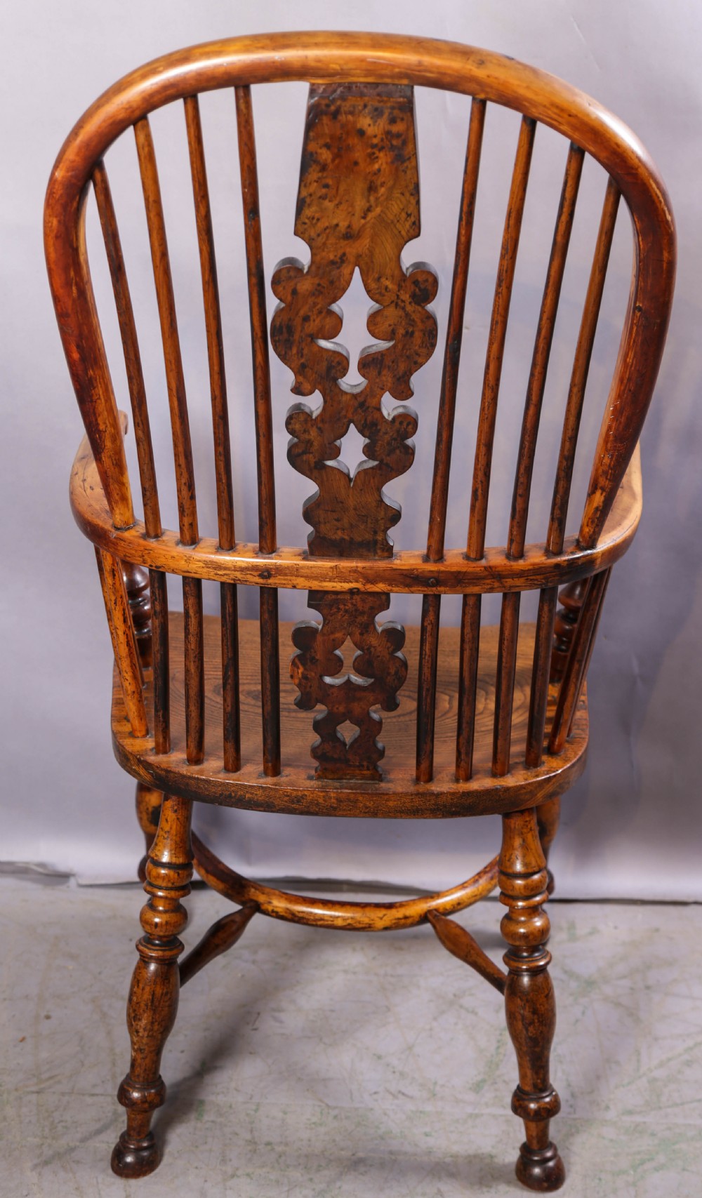 An antique yew wood high back Windsor armchair featuring a bow back, pierced central splat, shaped saddle seat, turned arm supports, turned legs, and a crinoline stretcher. View III
