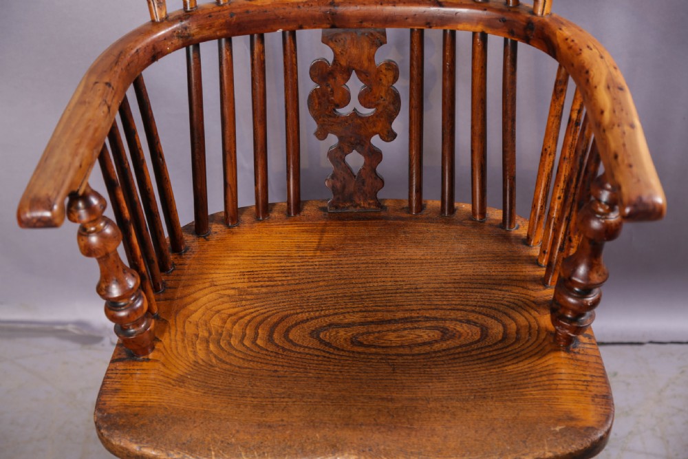 An antique yew wood high back Windsor armchair featuring a bow back, pierced central splat, shaped saddle seat, turned arm supports, turned legs, and a crinoline stretcher. View IV