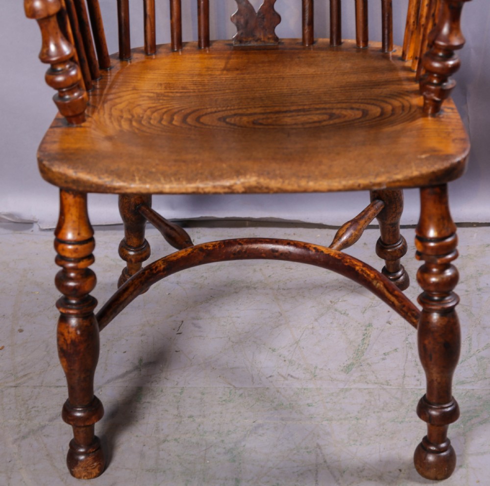 An antique yew wood high back Windsor armchair featuring a bow back, pierced central splat, shaped saddle seat, turned arm supports, turned legs, and a crinoline stretcher. View V