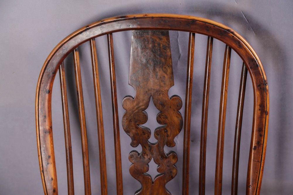 An antique yew wood high back Windsor armchair featuring a bow back, pierced central splat, shaped saddle seat, turned arm supports, turned legs, and a crinoline stretcher. View VI
