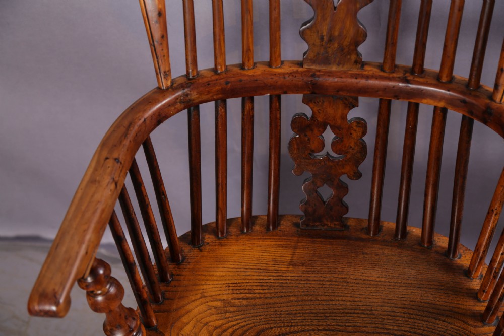 An antique yew wood high back Windsor armchair featuring a bow back, pierced central splat, shaped saddle seat, turned arm supports, turned legs, and a crinoline stretcher. View VIII