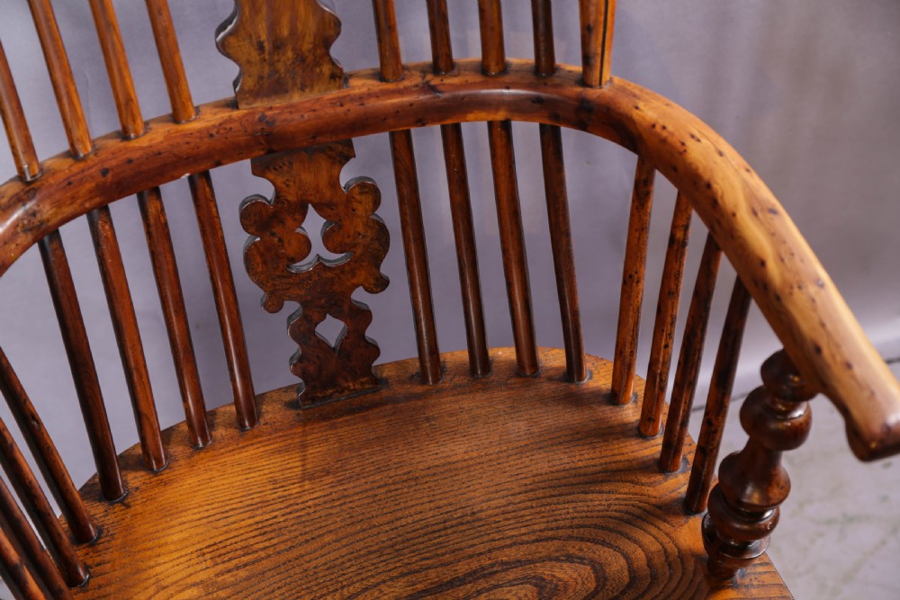 An antique yew wood high back Windsor armchair featuring a bow back, pierced central splat, shaped saddle seat, turned arm supports, turned legs, and a crinoline stretcher. View IX