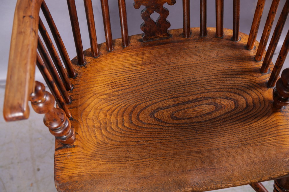 An antique yew wood high back Windsor armchair featuring a bow back, pierced central splat, shaped saddle seat, turned arm supports, turned legs, and a crinoline stretcher. View X