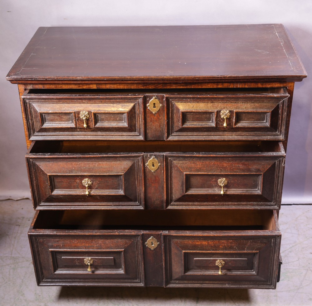 A dark brown George I oak chest of drawers featuring geometric panelled drawer fronts and brass drop handles. View III