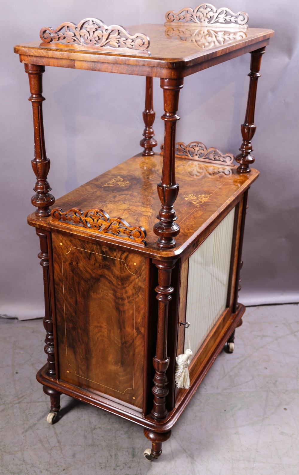 An antique Victorian burr walnut music cabinet featuring tiered shelves, marquetry inlay, turned columns, and a glazed door.