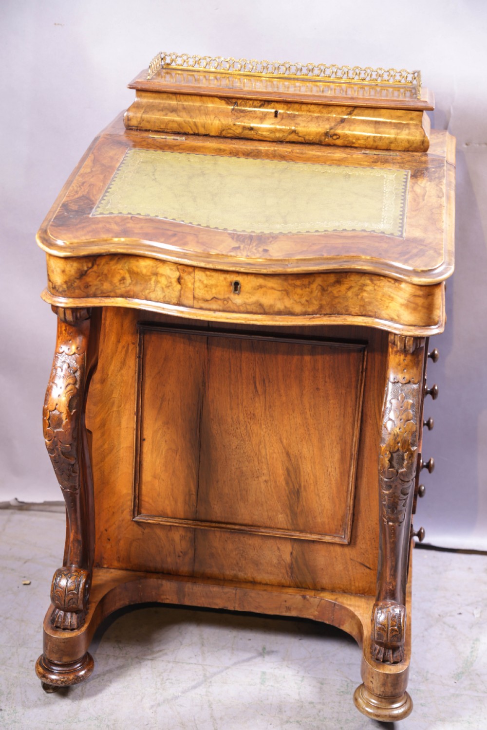 A Victorian burr walnut Davenport desk featuring a leather-inset sloping writing surface, brass gallery rail, and carved front supports.