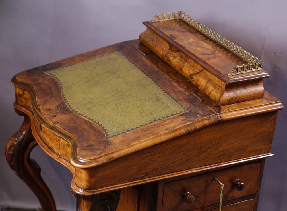 A Victorian burr walnut Davenport desk featuring a leather-inset sloping writing surface, brass gallery rail, and carved front supports. View V