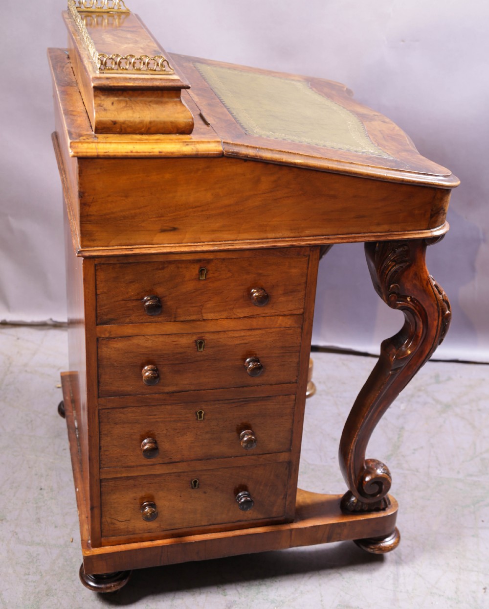 A Victorian burr walnut Davenport desk featuring a leather-inset sloping writing surface, brass gallery rail, and carved front supports. View X