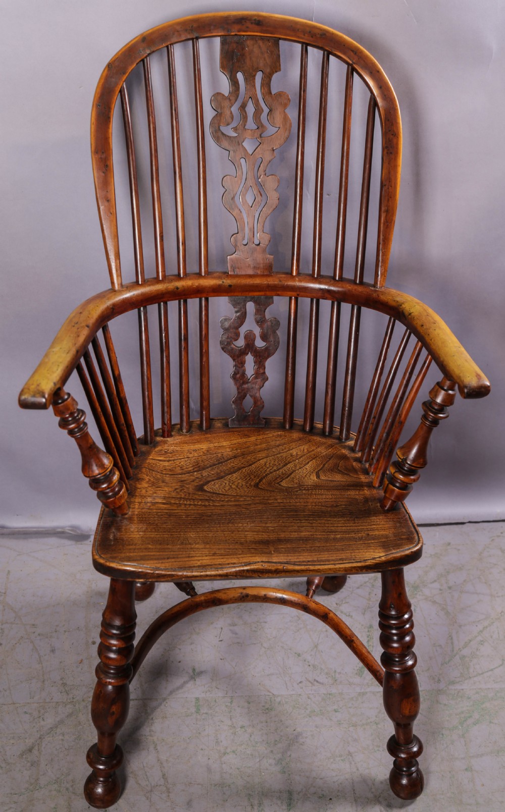 A 19th-century yew wood Windsor armchair featuring a bow back, ornate pierced splat, turned spindles, shaped seat, and turned legs.