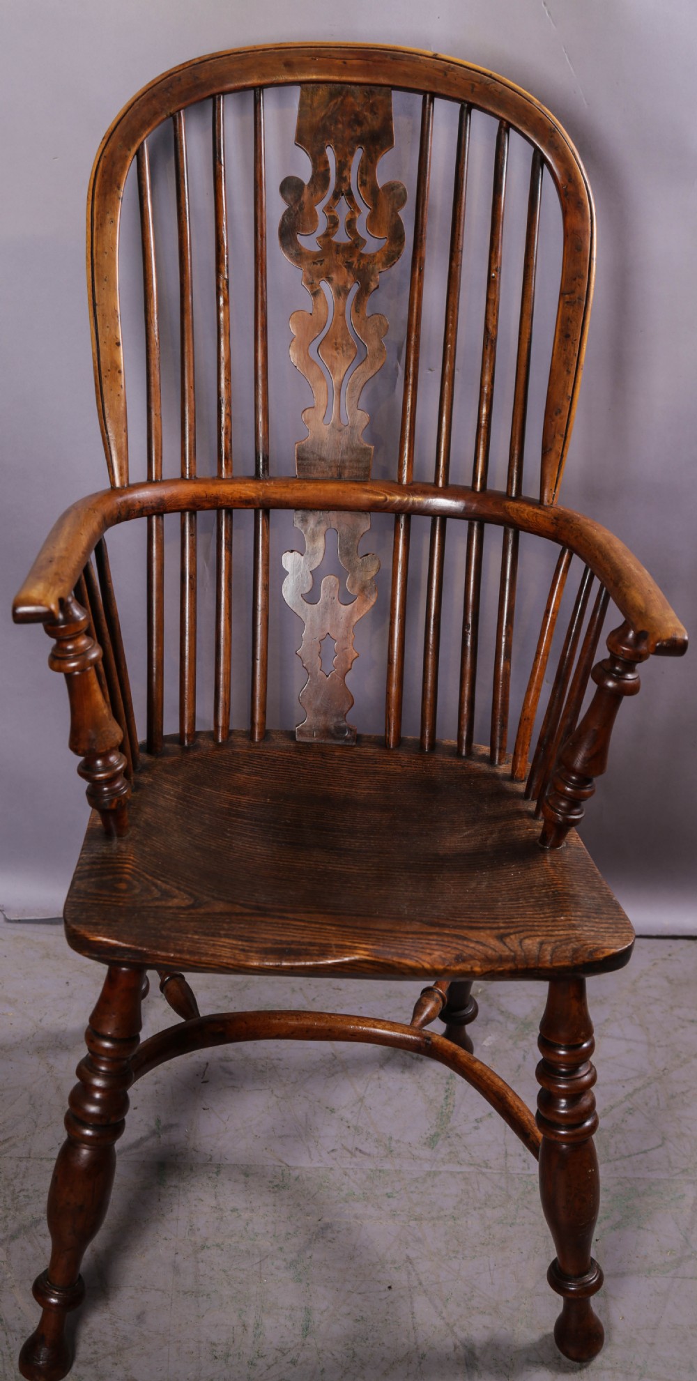 An antique yew wood high-back Windsor armchair featuring a pierced decorative splat, spindle back, shaped elm seat, turned legs, and a curved stretcher.