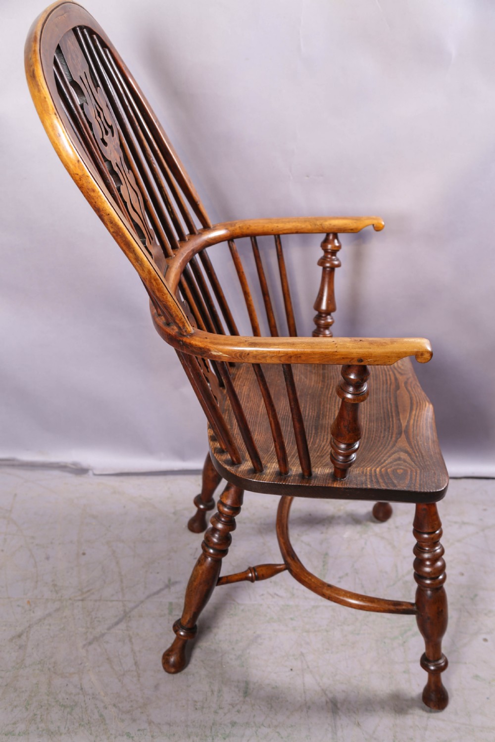 An antique yew wood high-back Windsor armchair featuring a pierced decorative splat, spindle back, shaped elm seat, turned legs, and a curved stretcher. View XII