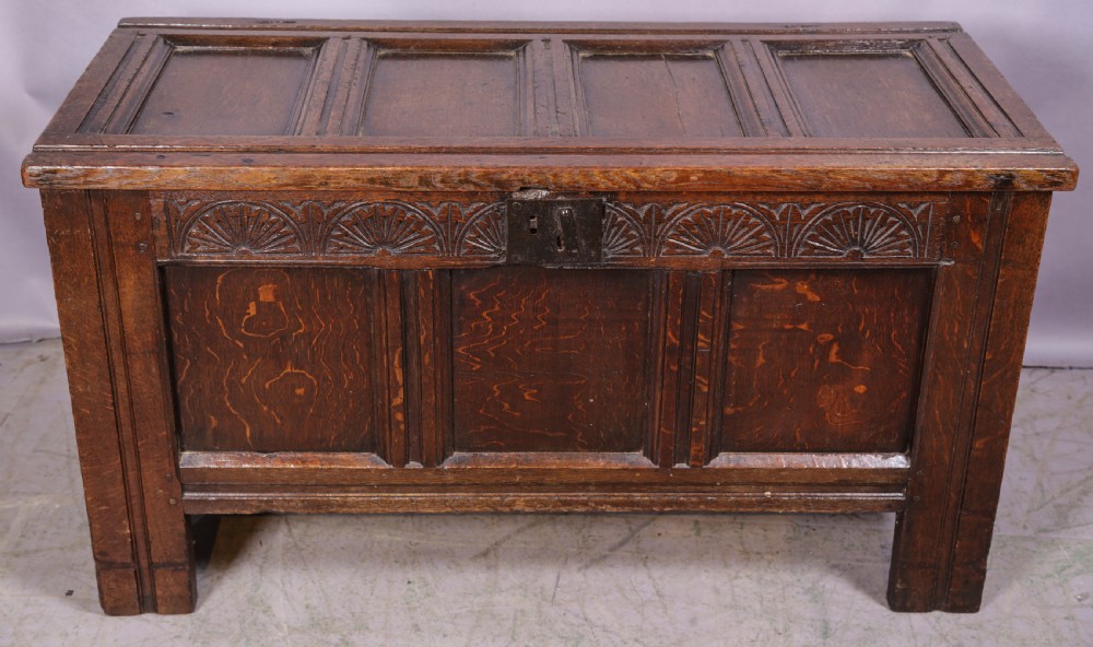 A 17th-century carved dark oak coffer featuring a four-panel hinged lid, a carved lunette frieze, three front panels, and a central iron escutcheon.