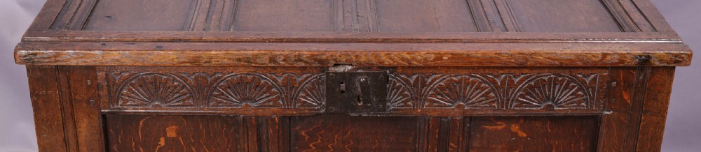A 17th-century carved dark oak coffer featuring a four-panel hinged lid, a carved lunette frieze, three front panels, and a central iron escutcheon. View II