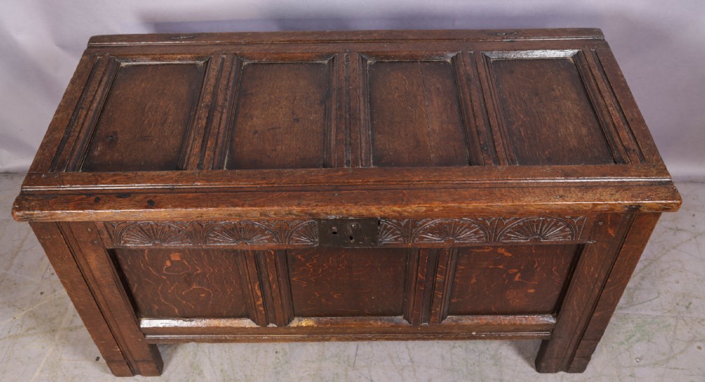 A 17th-century carved dark oak coffer featuring a four-panel hinged lid, a carved lunette frieze, three front panels, and a central iron escutcheon. View III