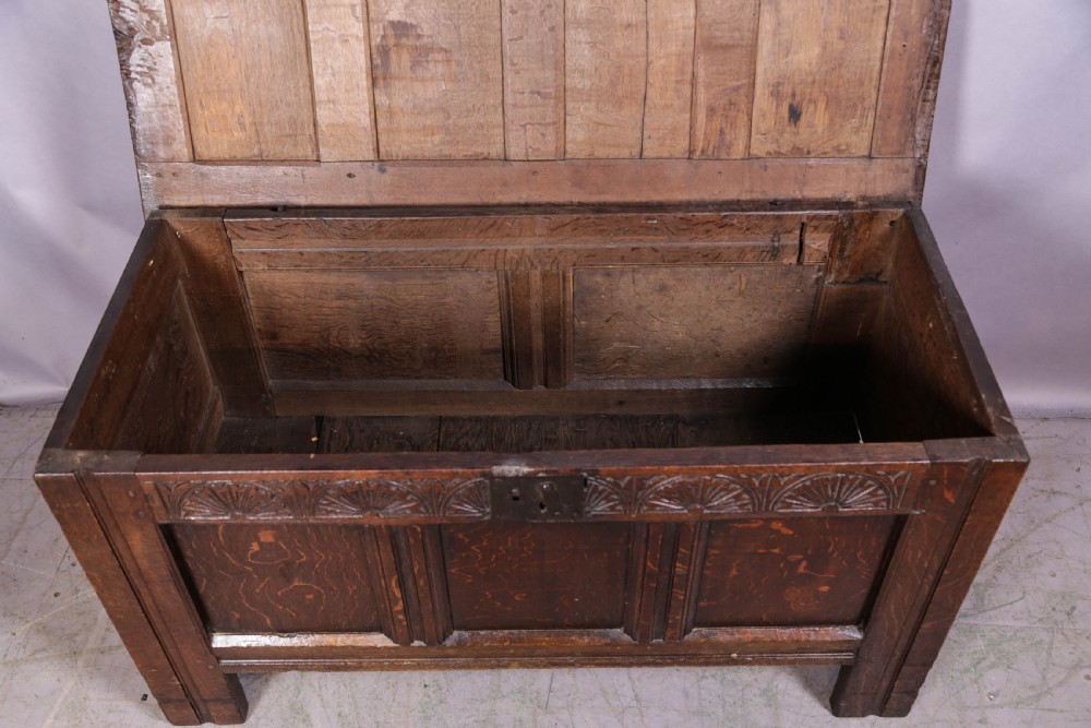 A 17th-century carved dark oak coffer featuring a four-panel hinged lid, a carved lunette frieze, three front panels, and a central iron escutcheon. View VI