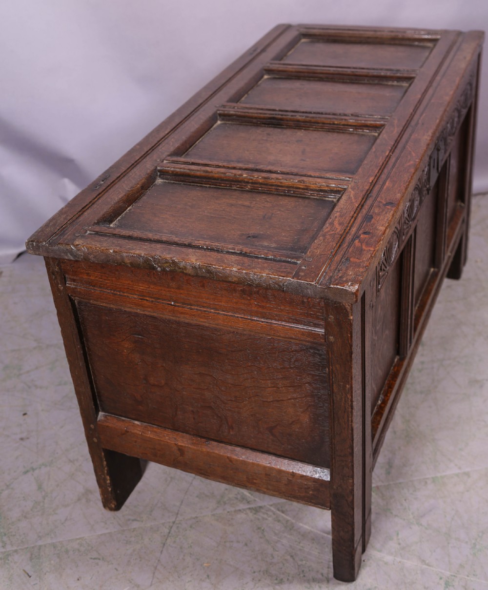A 17th-century carved dark oak coffer featuring a four-panel hinged lid, a carved lunette frieze, three front panels, and a central iron escutcheon. View VII
