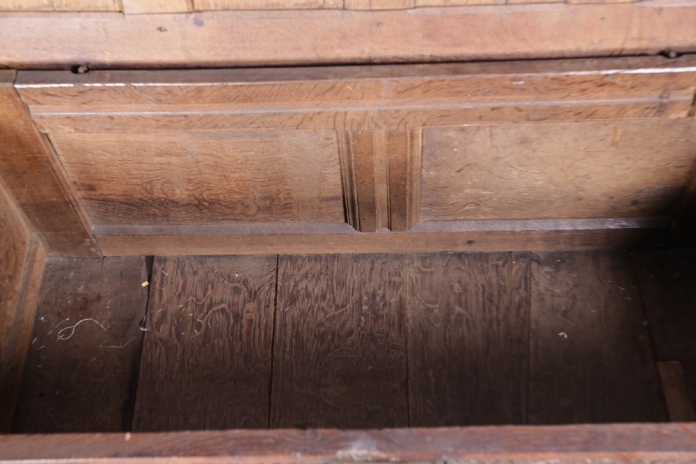 A 17th-century carved dark oak coffer featuring a four-panel hinged lid, a carved lunette frieze, three front panels, and a central iron escutcheon. View VIII