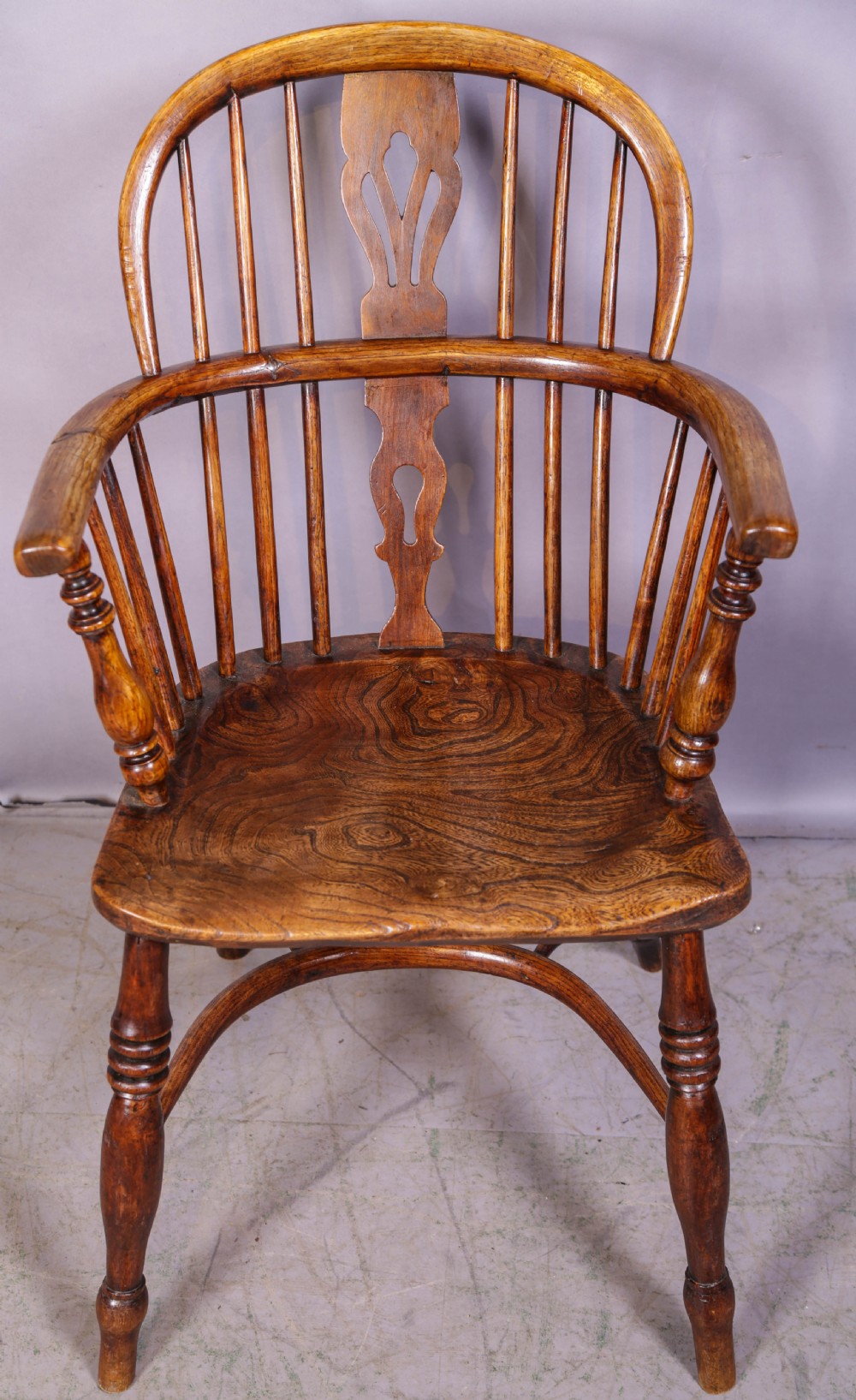 A low back ash and elm Windsor armchair featuring a shaped solid elm saddle seat, turned legs, curved stretcher, and a pierced splat back.