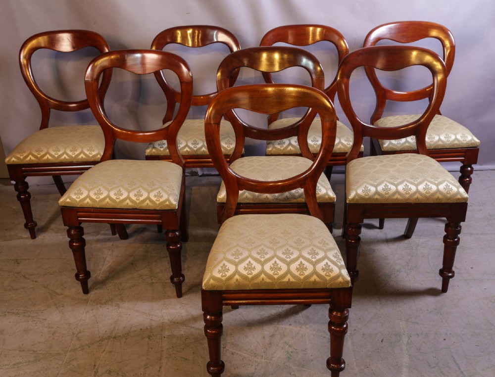 Set of eight Victorian mahogany dining chairs featuring rounded balloon backs, turned front legs, and patterned light-coloured upholstered seats.