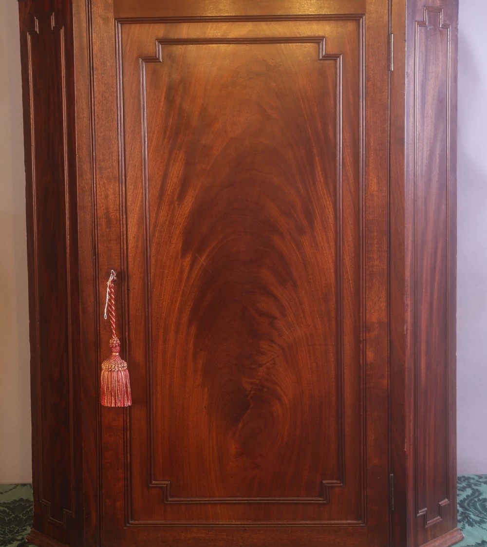 An antique Georgian flame mahogany corner cupboard featuring a swan-neck pediment with carved rosettes and a single panelled door. View II