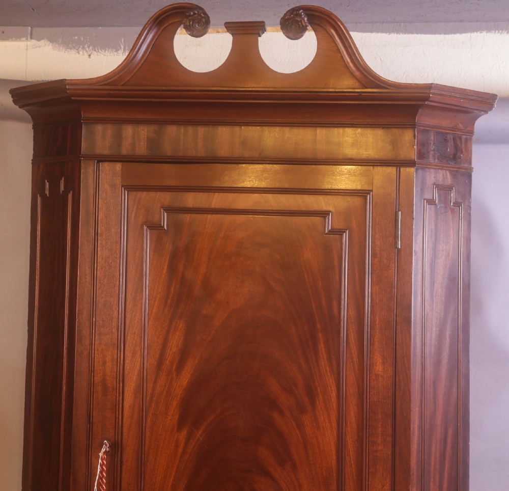 An antique Georgian flame mahogany corner cupboard featuring a swan-neck pediment with carved rosettes and a single panelled door. View III