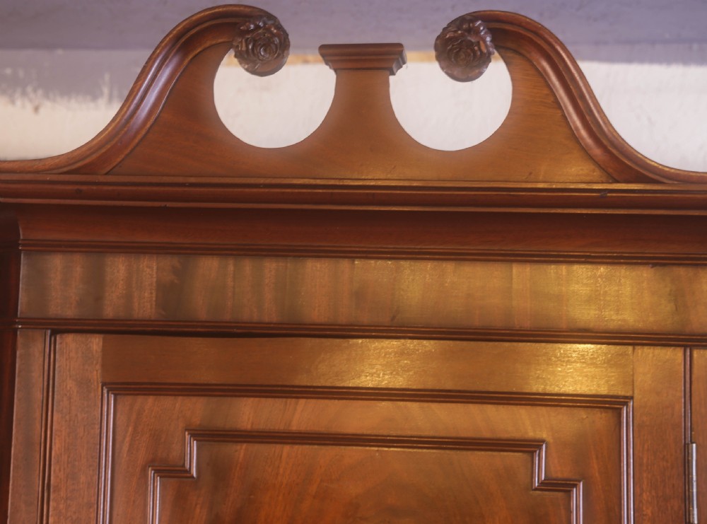 An antique Georgian flame mahogany corner cupboard featuring a swan-neck pediment with carved rosettes and a single panelled door. View IV