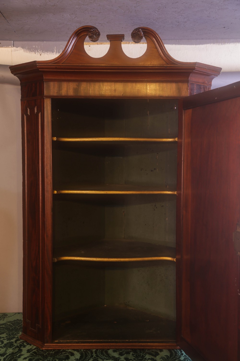An antique Georgian flame mahogany corner cupboard featuring a swan-neck pediment with carved rosettes and a single panelled door. View V