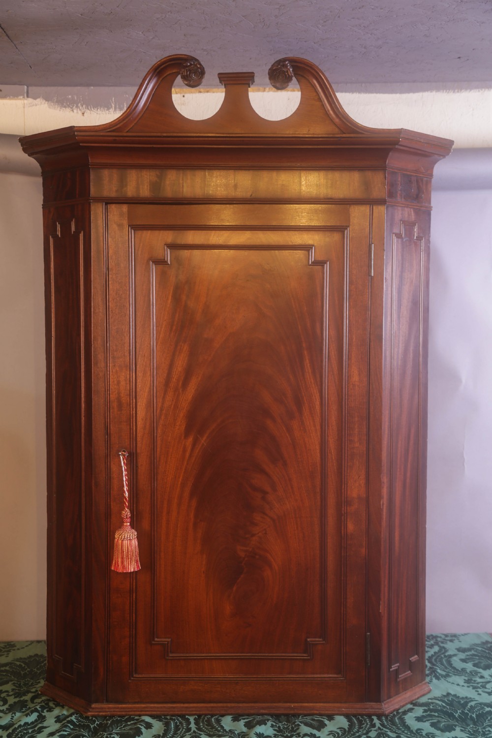 An antique Georgian flame mahogany corner cupboard featuring a swan-neck pediment with carved rosettes and a single panelled door. View VI