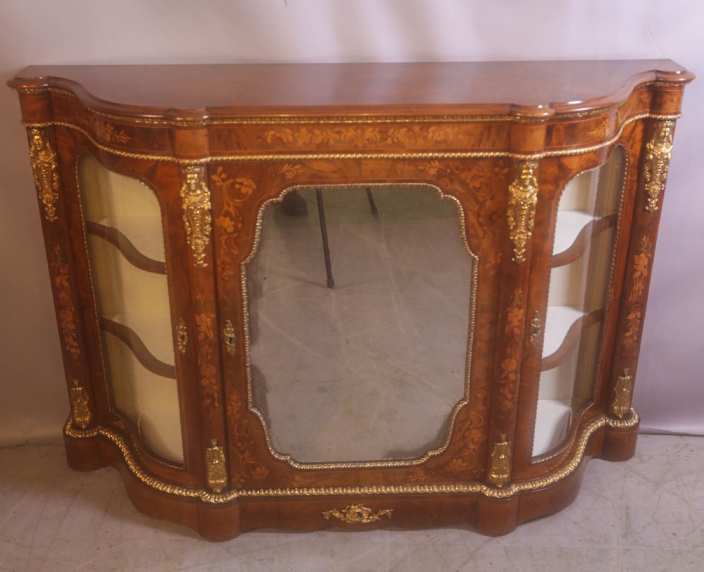 A Victorian burr walnut credenza featuring floral marquetry inlay, gilt-metal mounts, a central mirrored door, and curved glass side display compartments.