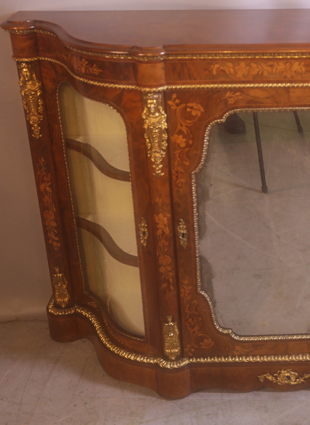 A Victorian burr walnut credenza featuring floral marquetry inlay, gilt-metal mounts, a central mirrored door, and curved glass side display compartments. View II