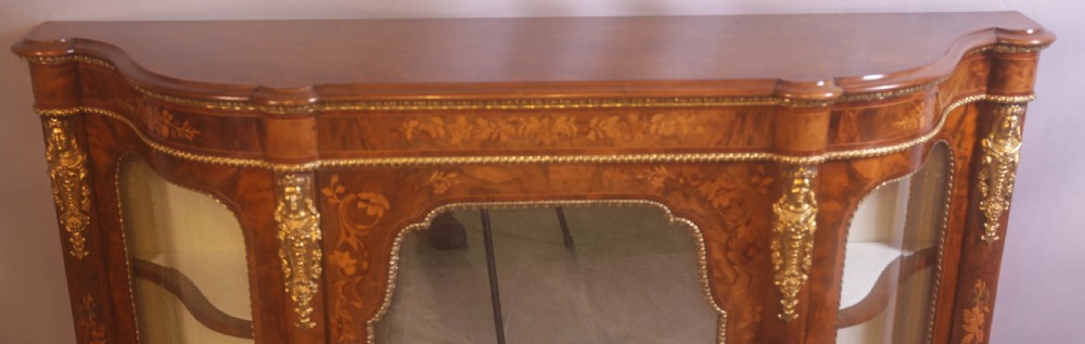 A Victorian burr walnut credenza featuring floral marquetry inlay, gilt-metal mounts, a central mirrored door, and curved glass side display compartments. View III