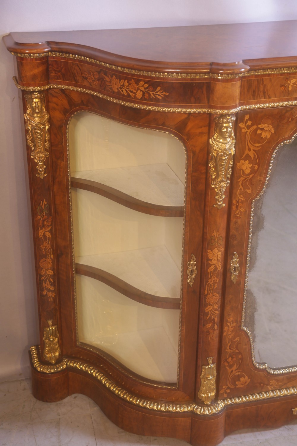 A Victorian burr walnut credenza featuring floral marquetry inlay, gilt-metal mounts, a central mirrored door, and curved glass side display compartments. View IV