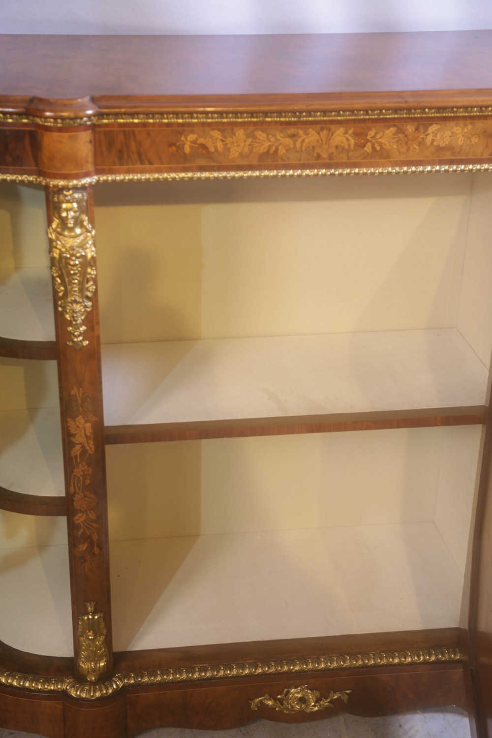 A Victorian burr walnut credenza featuring floral marquetry inlay, gilt-metal mounts, a central mirrored door, and curved glass side display compartments. View VI