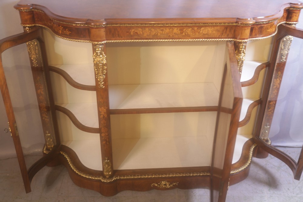 A Victorian burr walnut credenza featuring floral marquetry inlay, gilt-metal mounts, a central mirrored door, and curved glass side display compartments. View VII