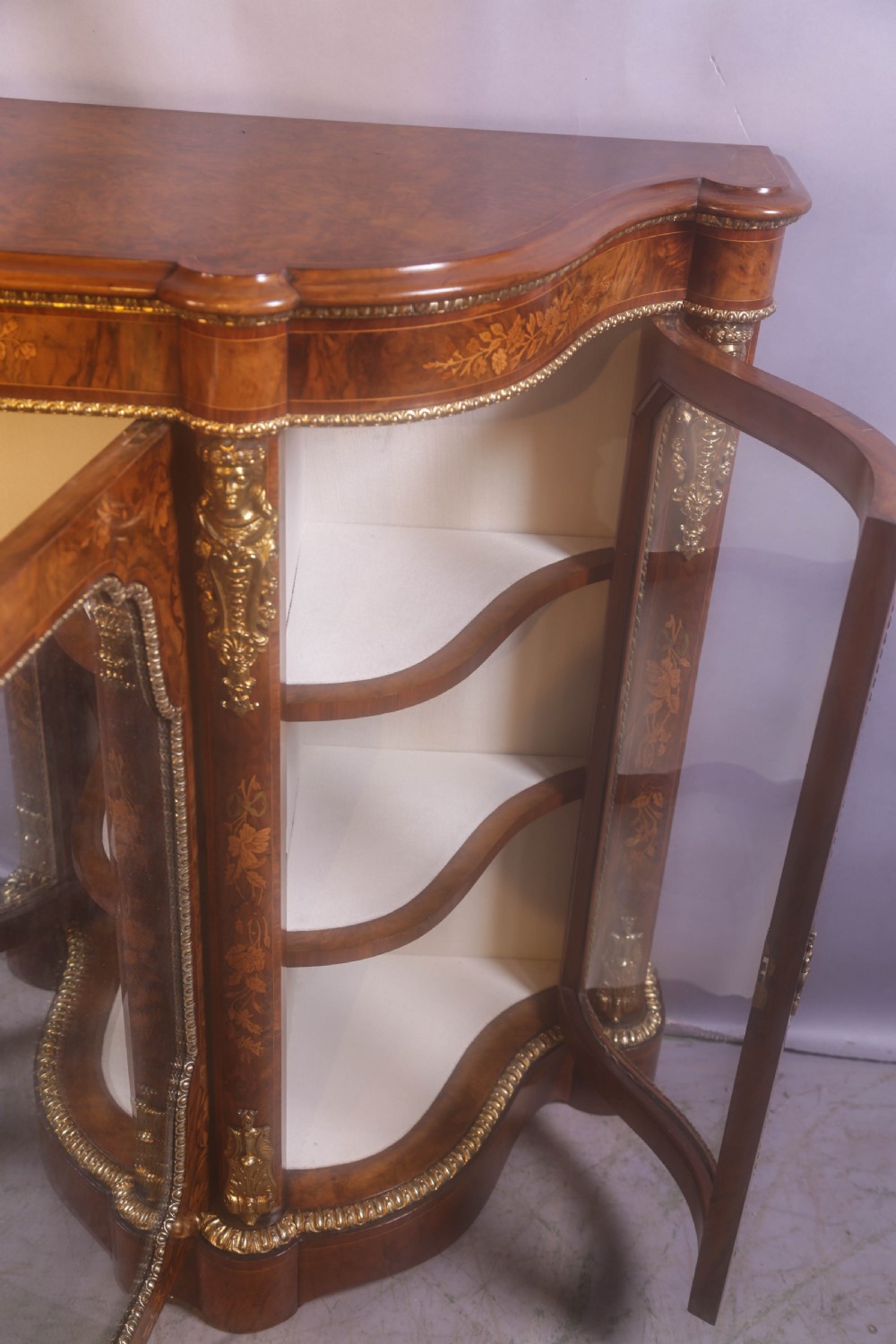 A Victorian burr walnut credenza featuring floral marquetry inlay, gilt-metal mounts, a central mirrored door, and curved glass side display compartments. View VIII