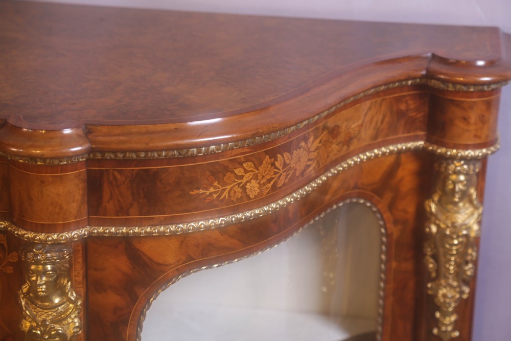 A Victorian burr walnut credenza featuring floral marquetry inlay, gilt-metal mounts, a central mirrored door, and curved glass side display compartments. View XI
