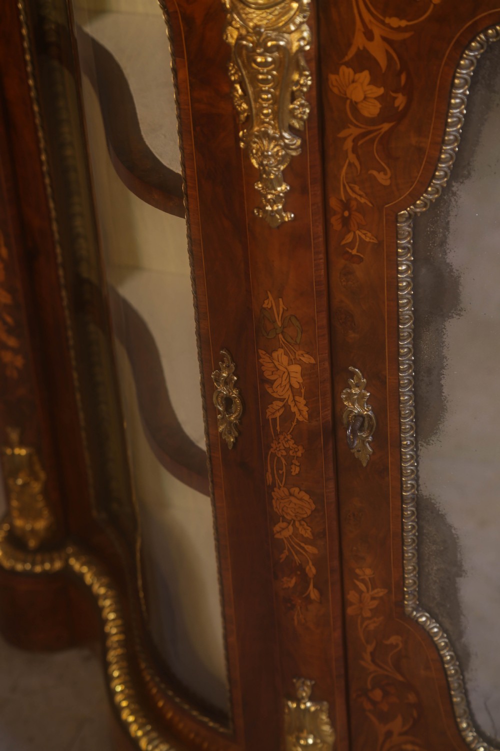 A Victorian burr walnut credenza featuring floral marquetry inlay, gilt-metal mounts, a central mirrored door, and curved glass side display compartments. View XIII