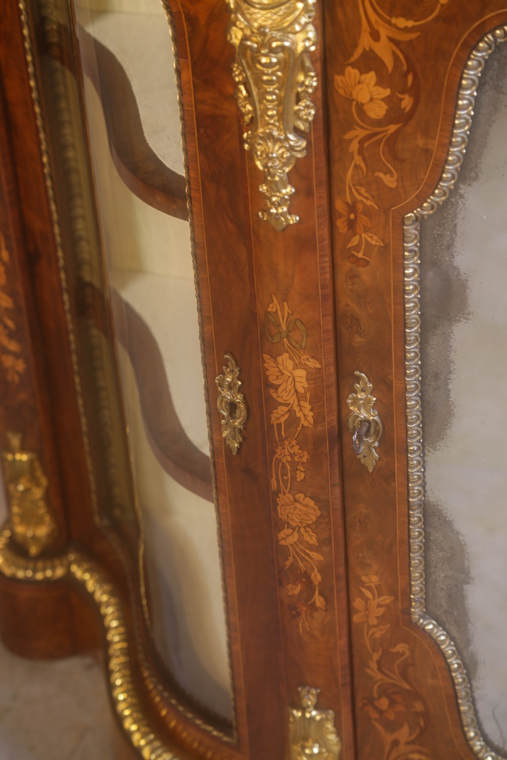 A Victorian burr walnut credenza featuring floral marquetry inlay, gilt-metal mounts, a central mirrored door, and curved glass side display compartments. View XIV