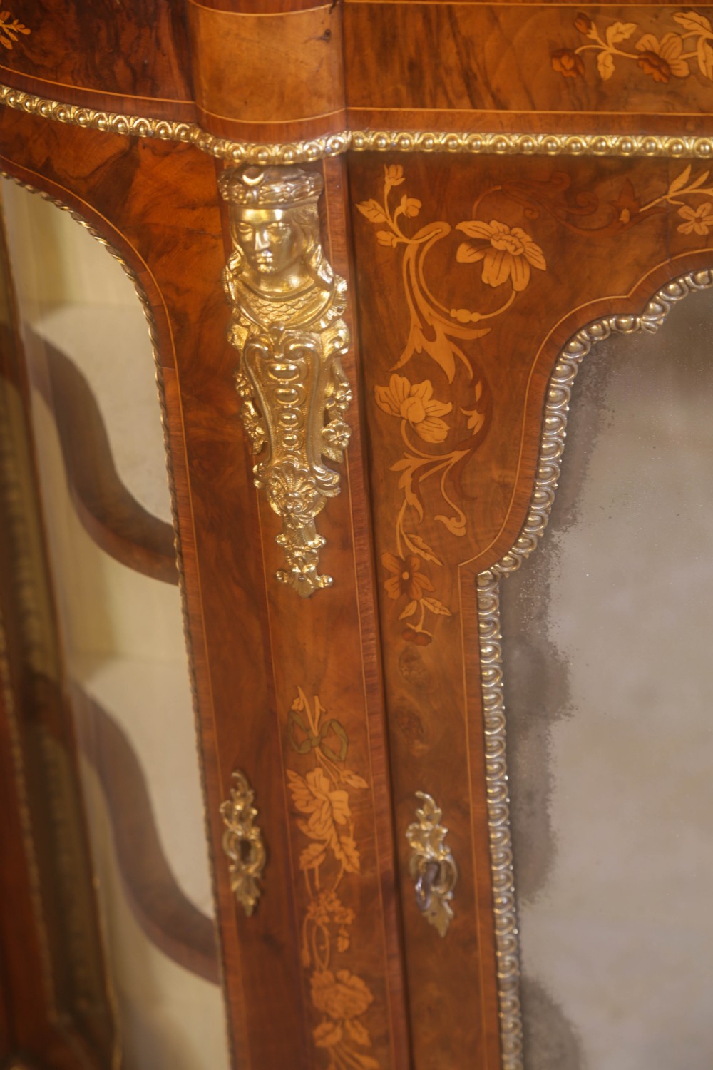 A Victorian burr walnut credenza featuring floral marquetry inlay, gilt-metal mounts, a central mirrored door, and curved glass side display compartments. View XV