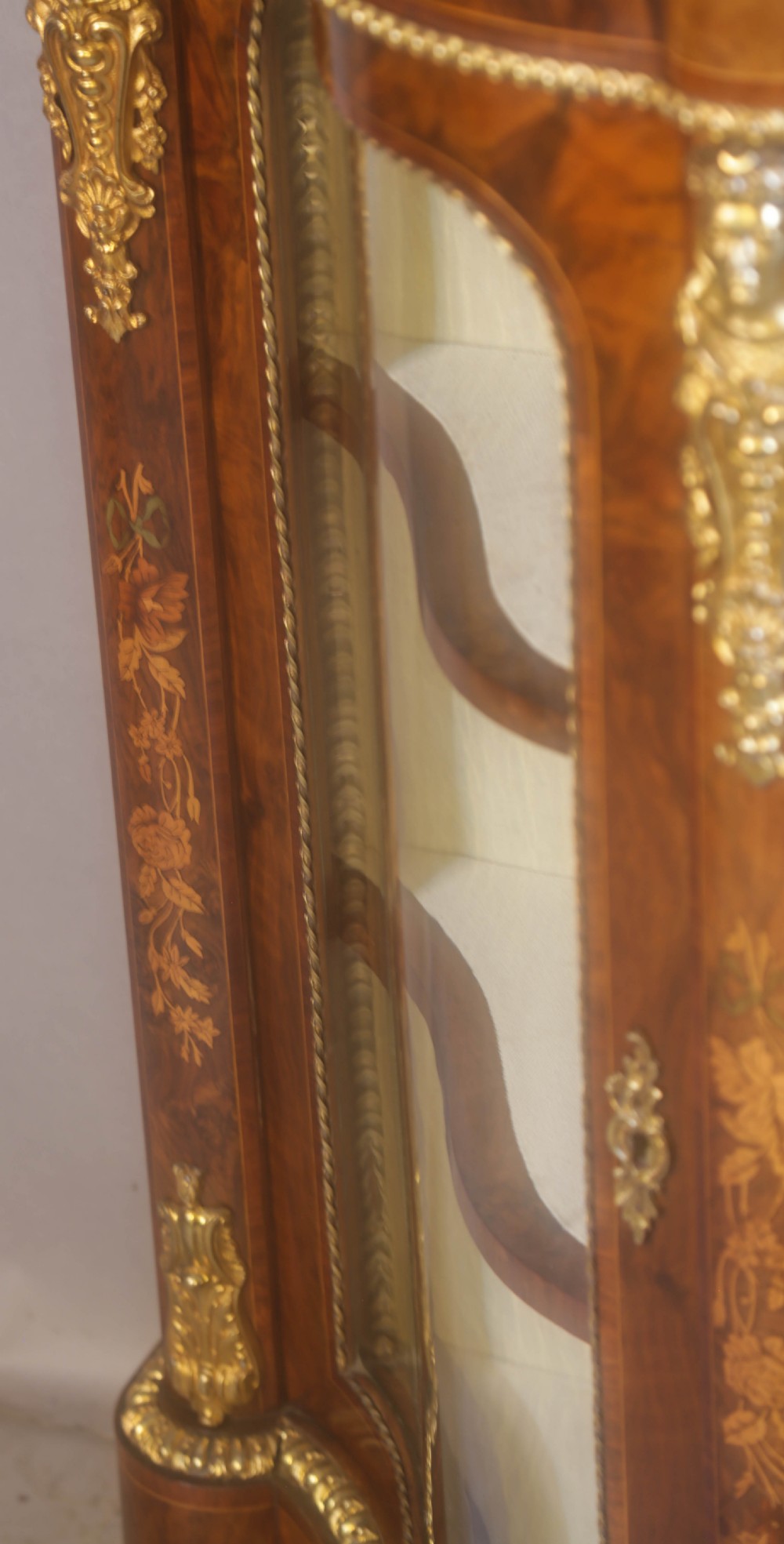 A Victorian burr walnut credenza featuring floral marquetry inlay, gilt-metal mounts, a central mirrored door, and curved glass side display compartments. View XVI
