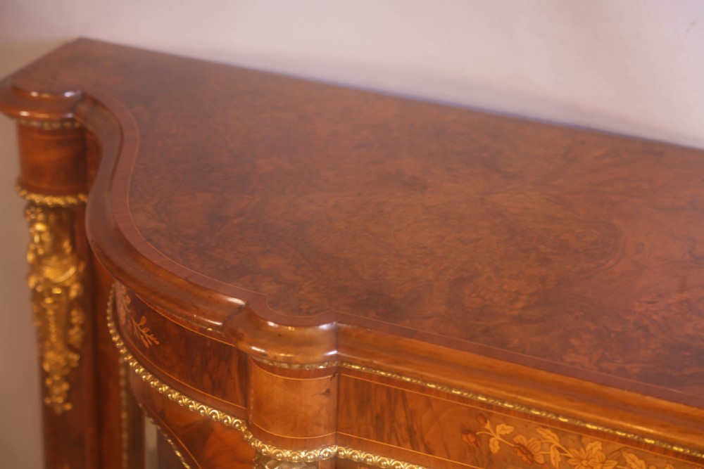 A Victorian burr walnut credenza featuring floral marquetry inlay, gilt-metal mounts, a central mirrored door, and curved glass side display compartments. View XVII