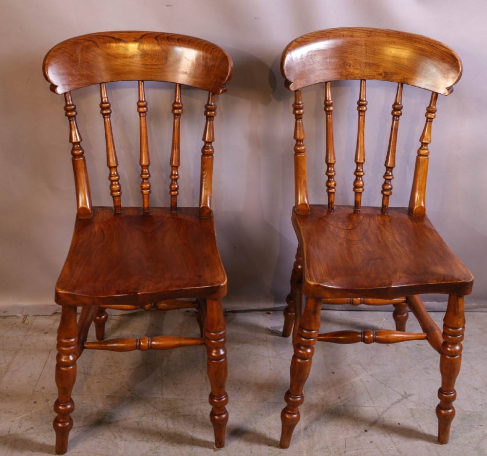 A set of four antique wooden kitchen chairs featuring rounded crest rails, turned back spindles, shaped solid seats, and turned legs. View V