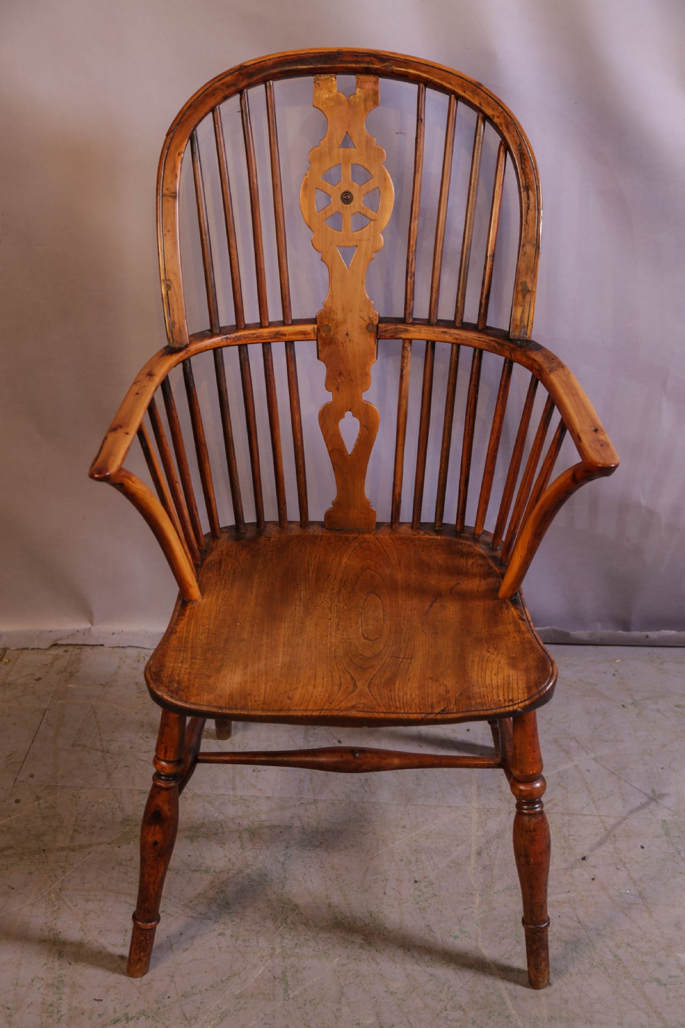 An antique Thames Valley yew wood Windsor armchair featuring a hoop back, central pierced wheel splat, contoured saddle seat, and turned legs.