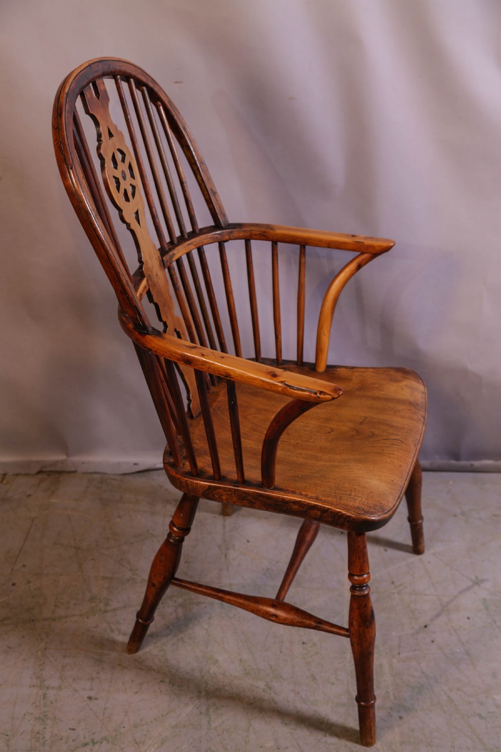 An antique Thames Valley yew wood Windsor armchair featuring a hoop back, central pierced wheel splat, contoured saddle seat, and turned legs. View II