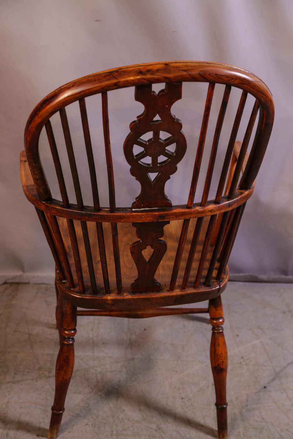 An antique Thames Valley yew wood Windsor armchair featuring a hoop back, central pierced wheel splat, contoured saddle seat, and turned legs. View III