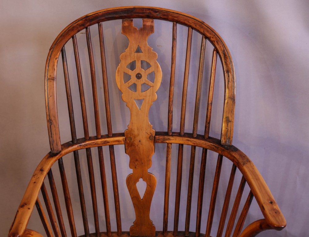 An antique Thames Valley yew wood Windsor armchair featuring a hoop back, central pierced wheel splat, contoured saddle seat, and turned legs. View VI