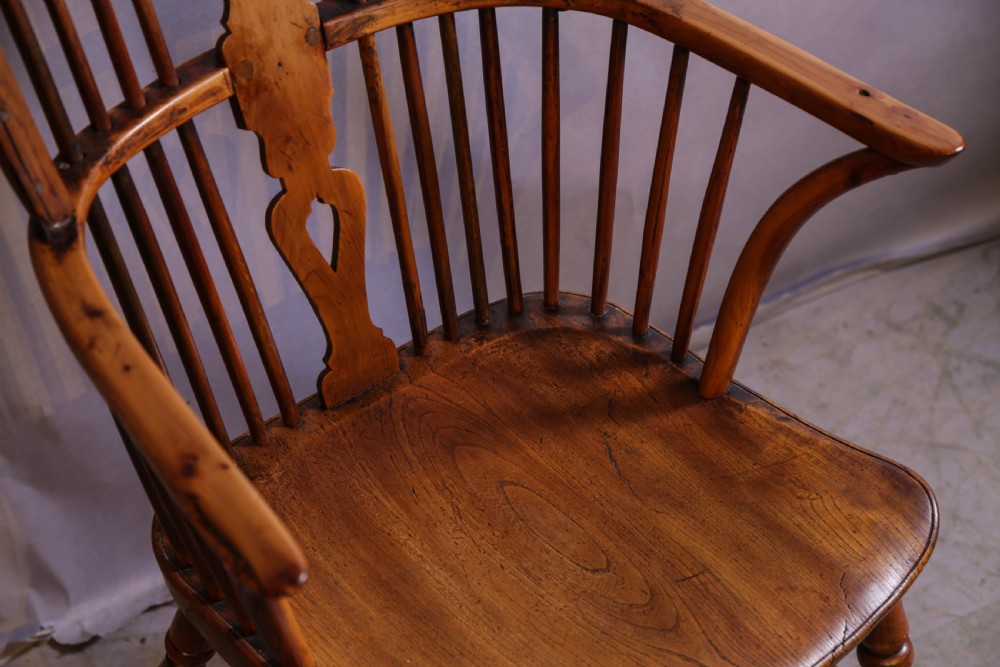 An antique Thames Valley yew wood Windsor armchair featuring a hoop back, central pierced wheel splat, contoured saddle seat, and turned legs. View X