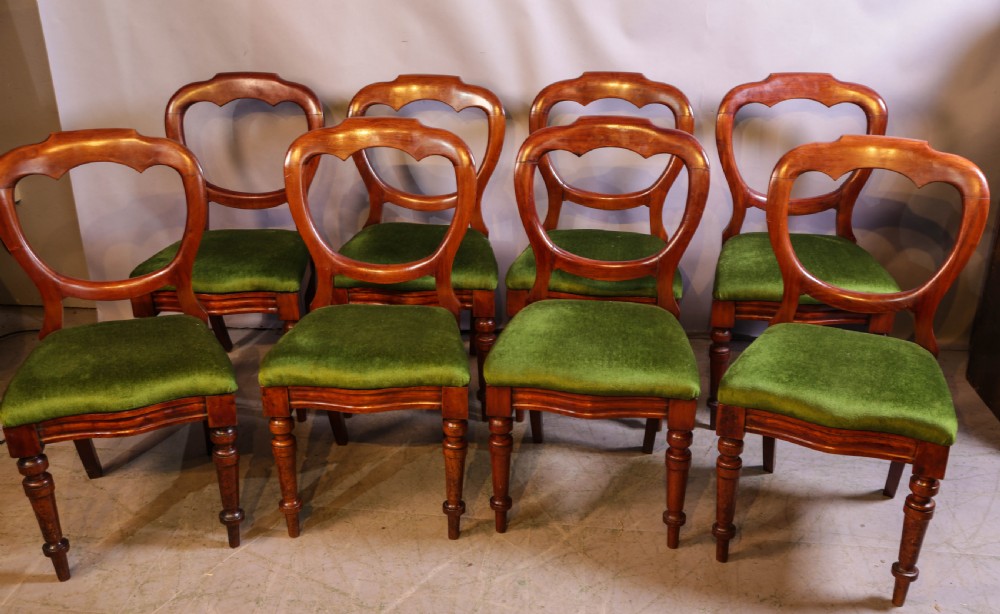 A set of eight Victorian mahogany balloon-back dining chairs with green velvet upholstered seats and turned front legs.