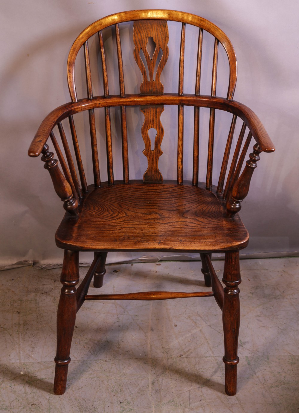 A wooden Windsor armchair featuring a steam-bent hoop back, pierced central splat, shaped elm seat, and turned legs.