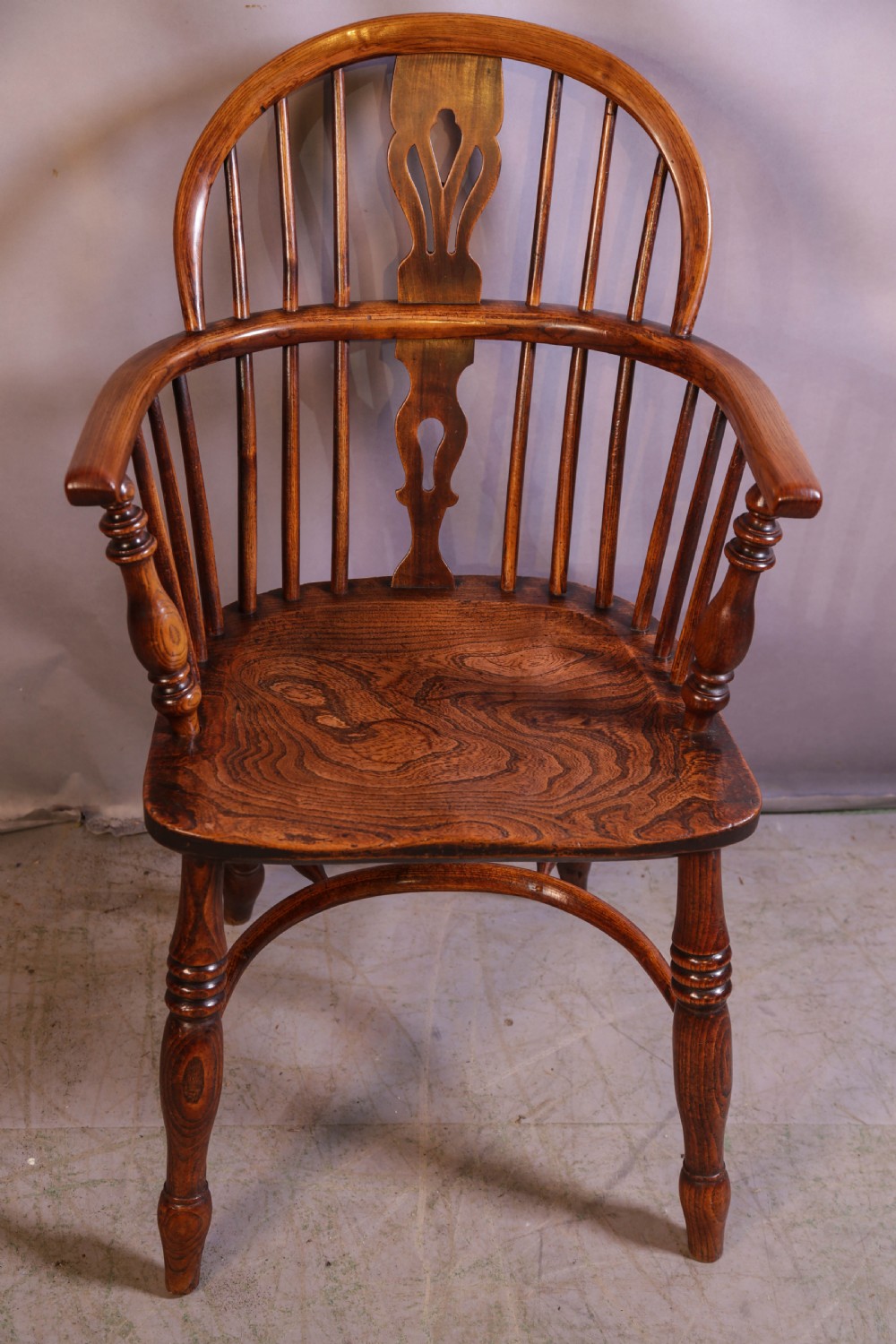 An English ash and elm Windsor armchair featuring a curved hoop back, pierced splat, turned spindles, contoured seat, and turned legs.
